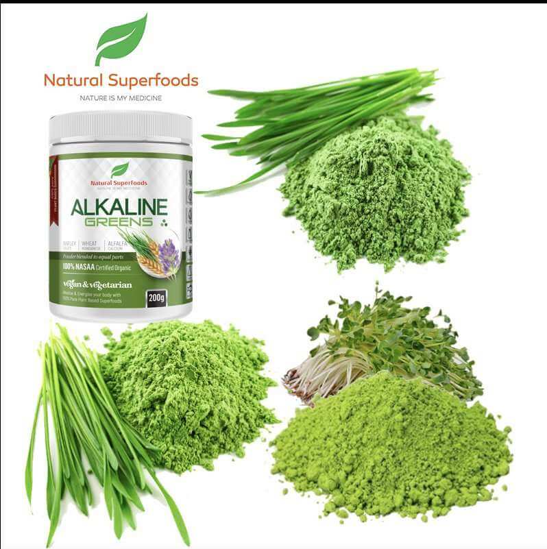 A white plastic jar labeled 'Natural Superfoods ALKALINE GREENS' surrounded by green chives, green powder, and microgreens on a white background.